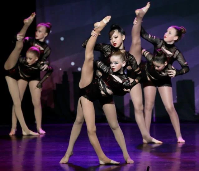 JMDS jazz dancers in black mesh costumes performing high kicks on stage