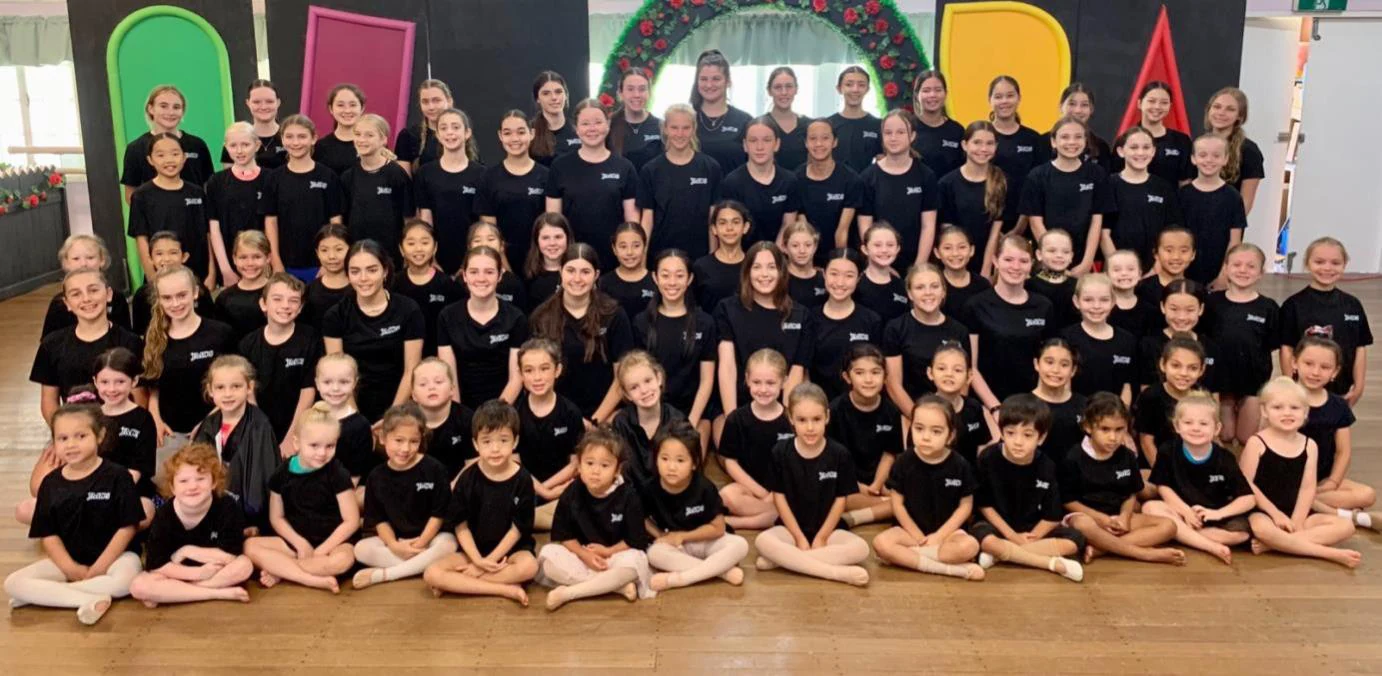 The whole JMDS school, dozens of students in black JMDS t-shirts, sitting together in the studio